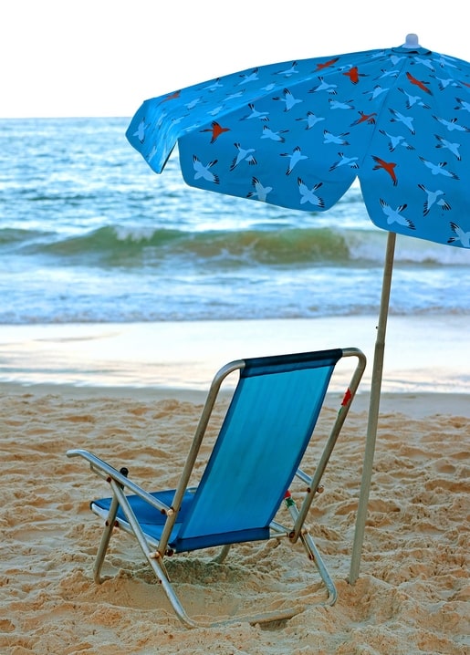 Empty blue beach chair under a bird-print umbrella facing the sea