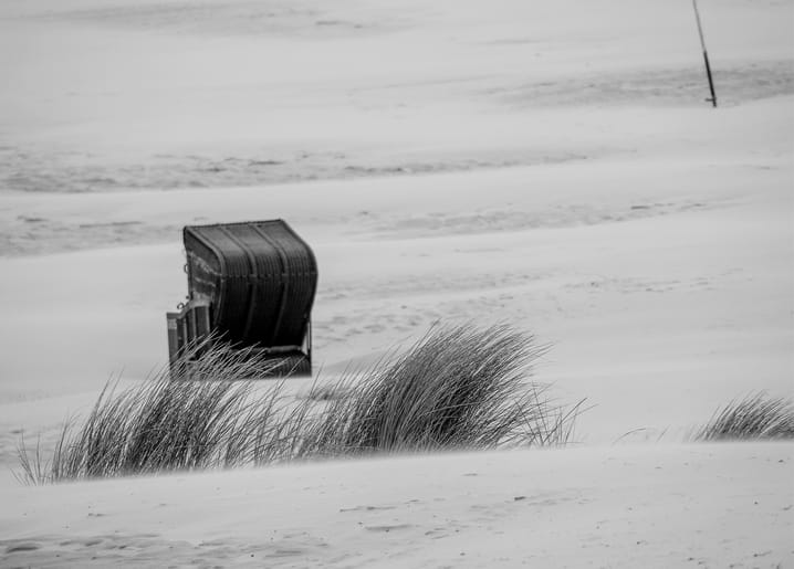 Roofed wicker beach chair standing alone in windswept dune grass on a foggy shore