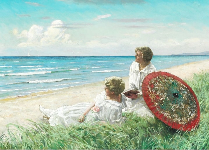 Zwei Frauen ruhen am Strand, eine liest neben einem geöffneten roten Sonnenschirm am Meer
