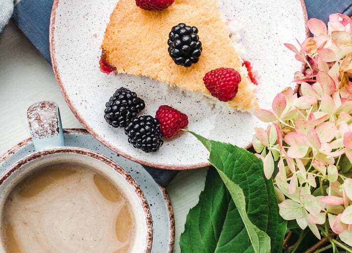 Stück Beeren-Biskuitkuchen mit Kaffeetasse und rosa Hortensienblüten