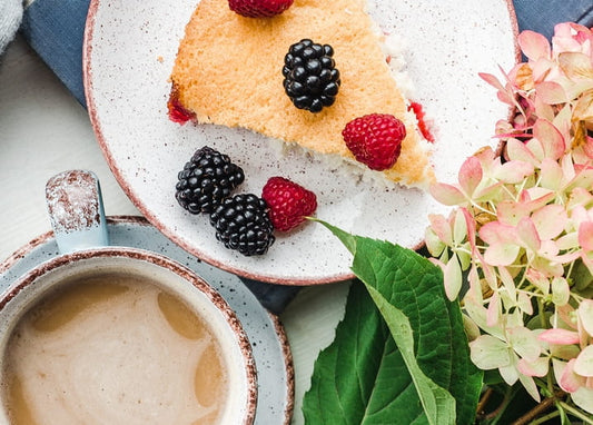Stück Beeren-Biskuitkuchen mit Kaffeetasse und rosa Hortensienblüten