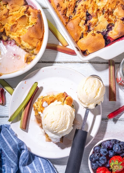 Two cobblers with rhubarb and berries served with scoops of melting vanilla ice cream