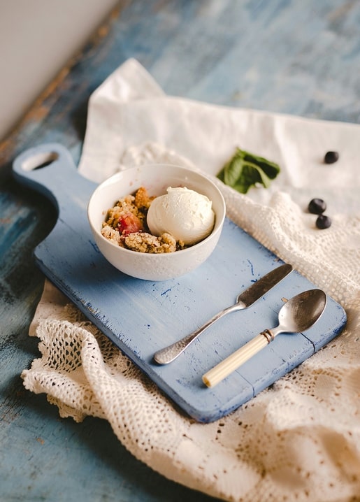 Bowl of berry crumble with vanilla ice cream on a rustic blue wooden board