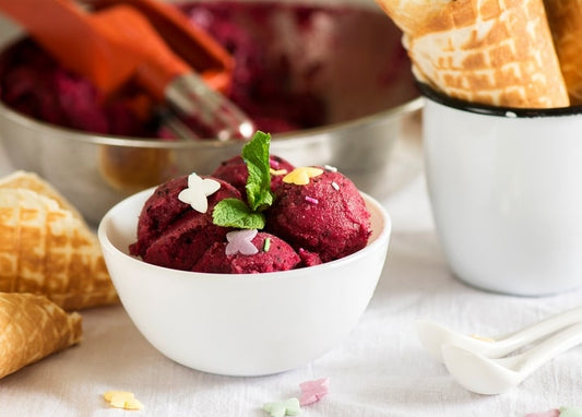 Scoops of berry ice cream with mint leaf and pastel butterfly sprinkles in a white bowl, waffle cones nearby