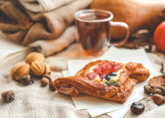 Blätterteig-Gebäck mit Erdbeeren und Blaubeeren neben einer Tasse Tee, Walnüssen, Eicheln und einem kleinen Kürbis
