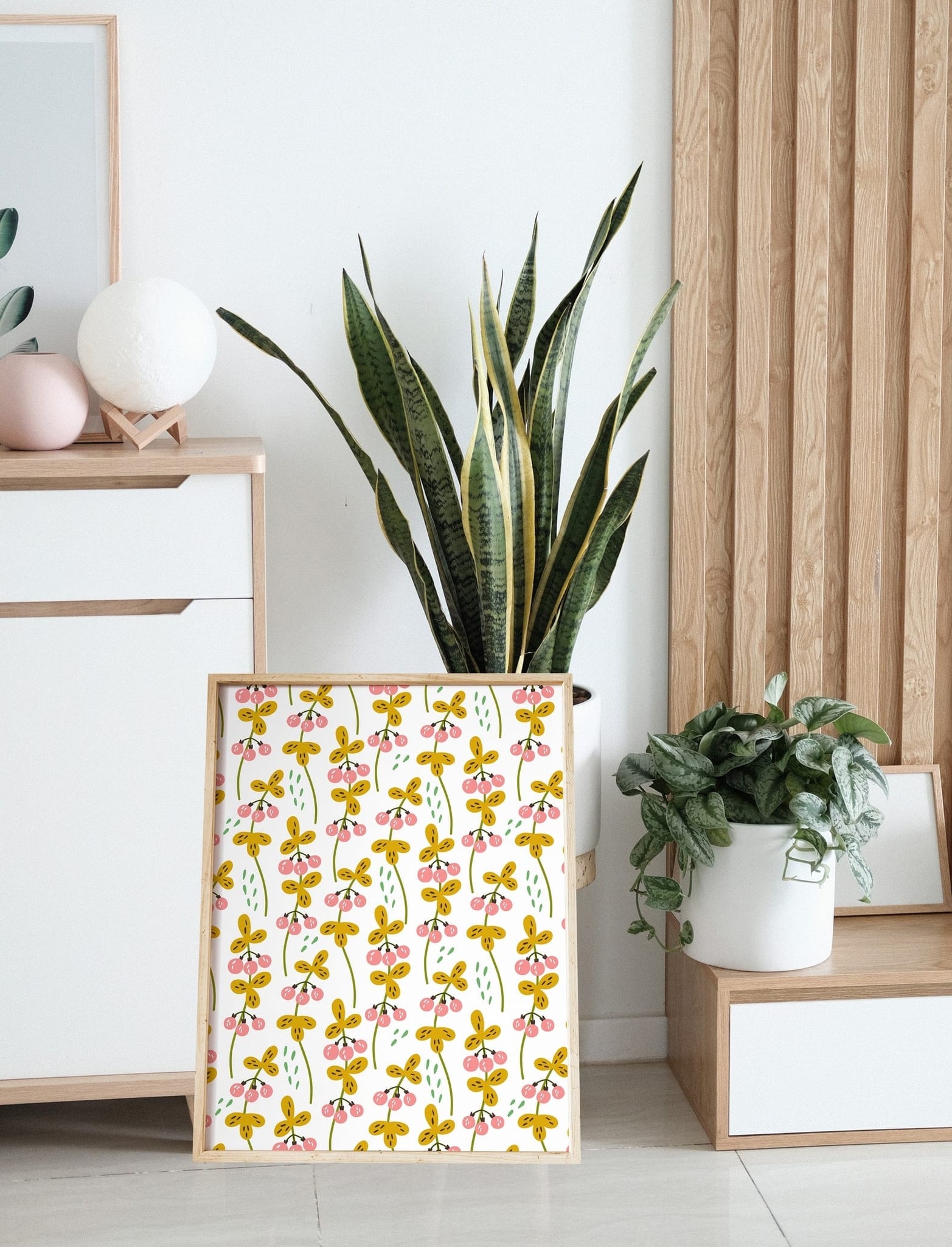 Framed berry pattern poster leaning against a dresser beside houseplants