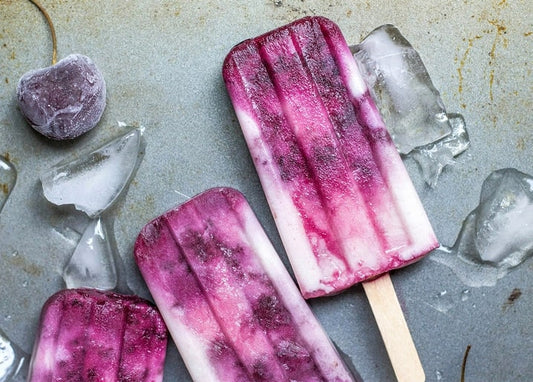 Berry ombre popsicles on crushed ice beside a single frozen cherry