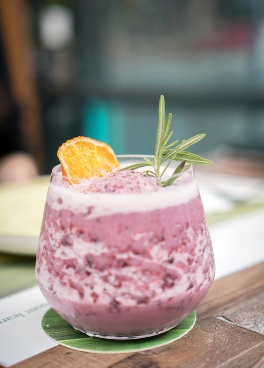 Purple berry smoothie garnished with a dried orange wheel and rosemary sprig