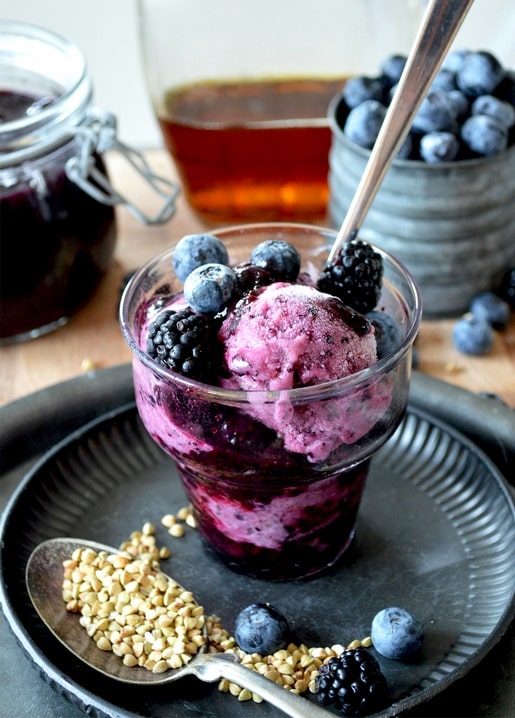 Glass of deep purple berry sorbet topped with blackberries and blueberries, honey jar and buckwheat spoon nearby
