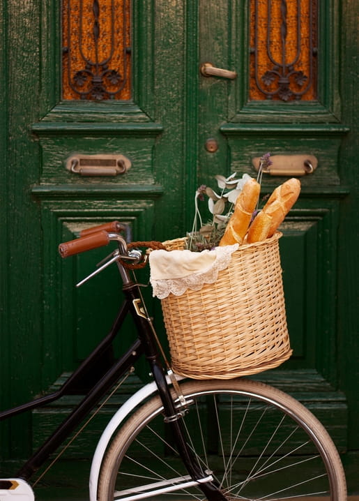 Wicker bicycle basket full of baguettes and lavender against a green door