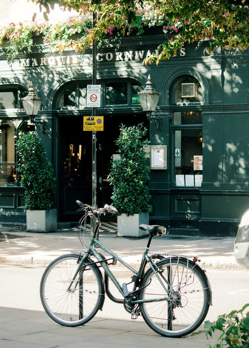Vintage bicycle parked by a lamppost outside a dark-green pub with hanging flower baskets.