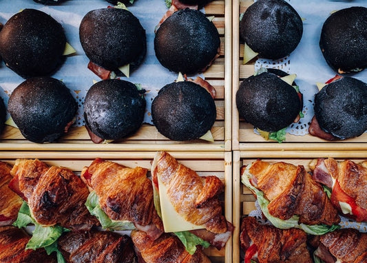 Schwarze Burger-Buns und Bacon-Käse-Croissants auf Holztabletts, von oben fotografiert