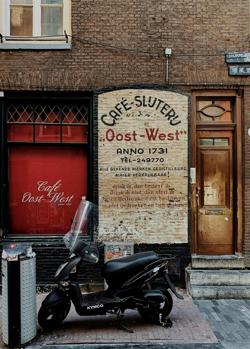 Black moped parked outside a weathered brick café with a hand-painted vintage sign