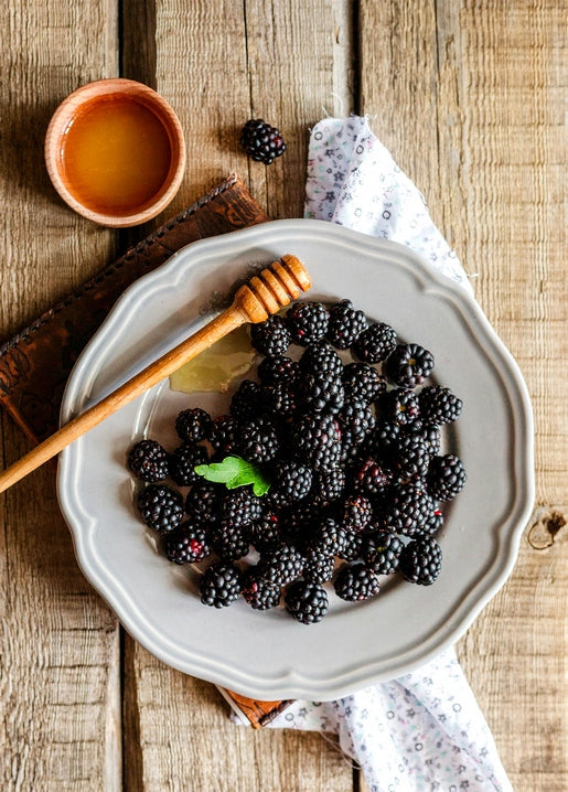 Plate of ripe blackberries with a honey dipper and bowl of honey