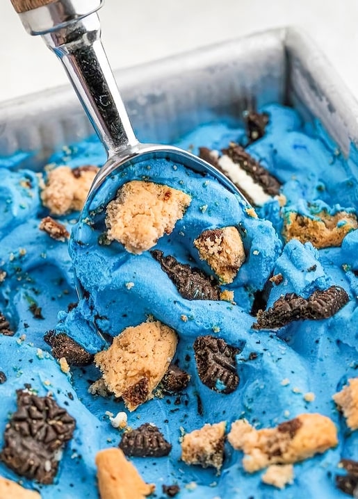 Scoop digging into blue cookie-dough ice cream with chocolate cookie pieces