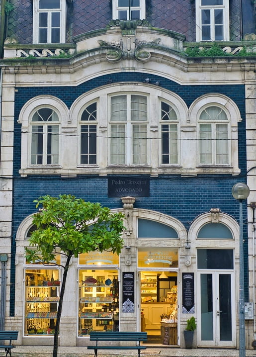 Blaue Azulejo-Fassade mit Bogenfenstern und erleuchtetem Eckladen in der Abenddämmerung