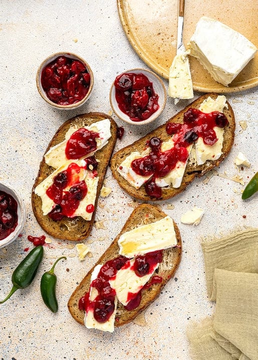 Toasted bread slices topped with brie cheese and cranberry sauce, served with jalapeño peppers