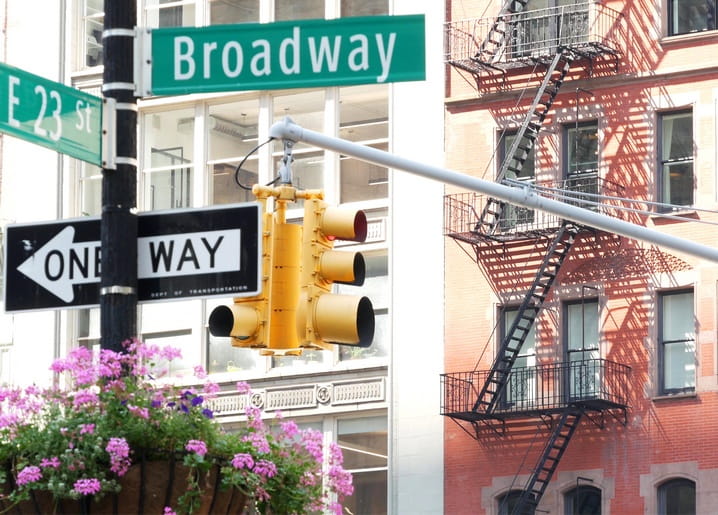 Broadway-Schild über einer Ampel mit Feuertreppe im Hintergrund