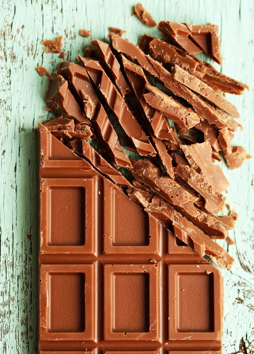 Milchschokoladenriegel in glänzende Stücke zerbrochen auf mintgrünem Tisch