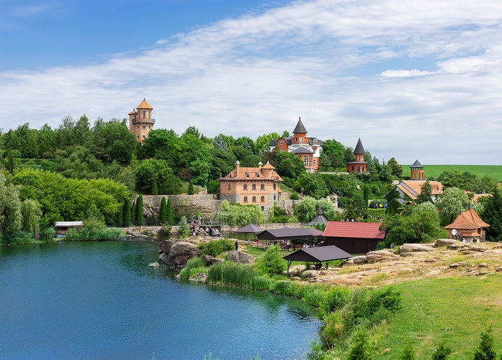 Turreted castle estate with red roofs above a rocky lake shore in Kyiv region