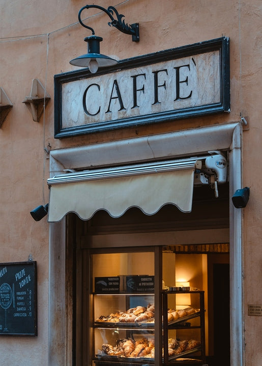 Cream awning below a hand-painted CAFFÈ sign, with pastries displayed in the café window