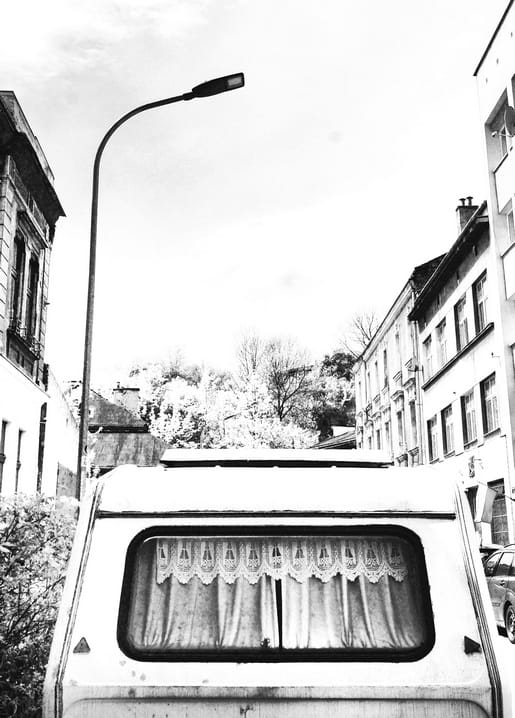 Schwarzweißfoto eines Campingbus-Fensters mit Spitzengardinen auf einer europäischen Straße