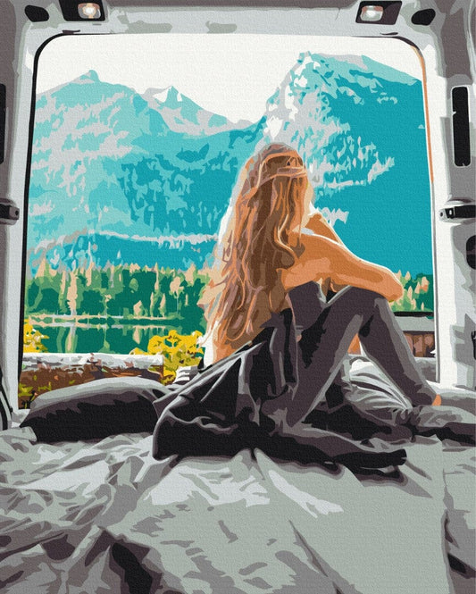 Frau in eine Decke gehüllt sitzt im Kofferraum eines Campervans mit Blick auf einen türkisfarbenen Bergsee