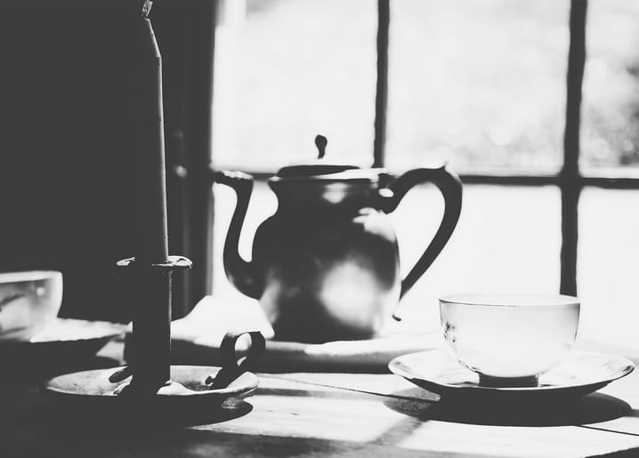 Schwarzweißes Stillleben mit Kerze, Teekanne und Teetasse am Fenster