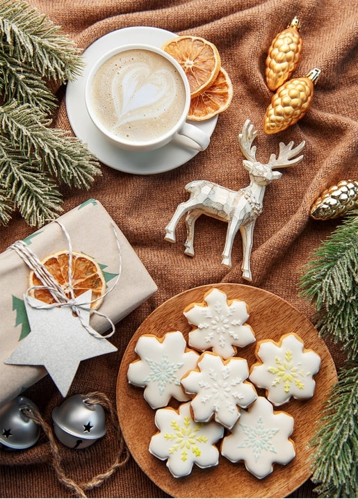 Flat lay of cappuccino, deer figurine, snowflake cookies and a wrapped gift on a knit blanket
