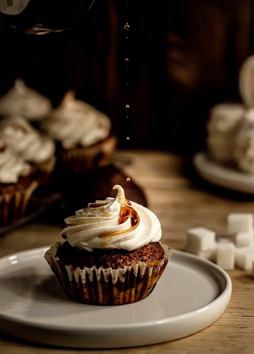 Schokoladen-Cupcake mit Baiser-Topping und Karamell, daneben Zuckerwürfel auf einem weißen Teller