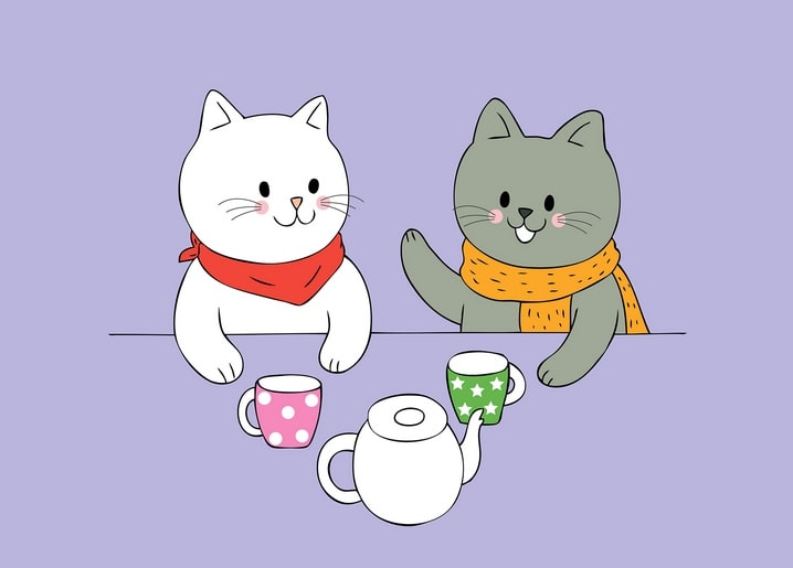 White and gray cats in scarves sharing tea at a table