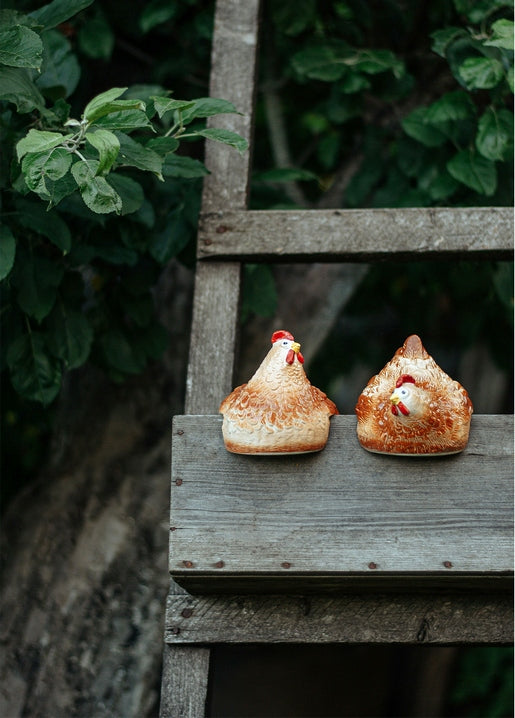 Two hand-painted ceramic hen figurines on a weathered wooden ladder in a garden
