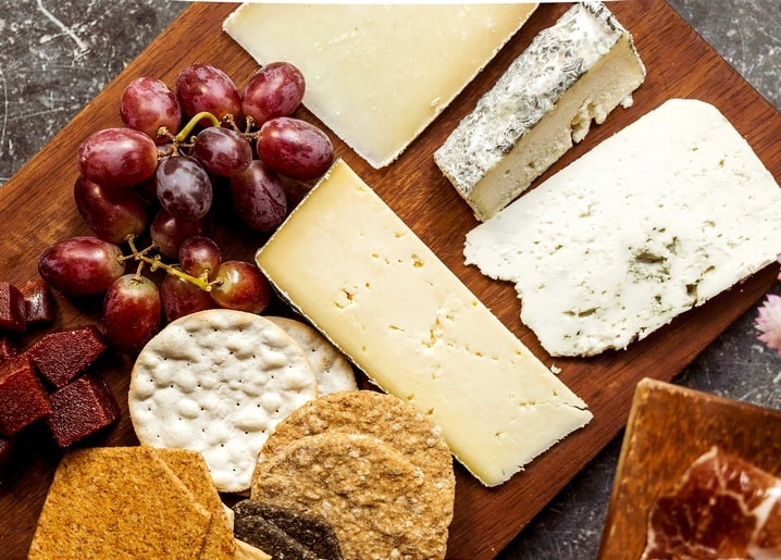 Käsestücke, rote Weintrauben, Cracker und Rohschinken auf einem dunklen Holzbrett
