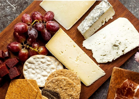 Cheese wedges, red grapes, crackers, and cured meat on a dark wooden board