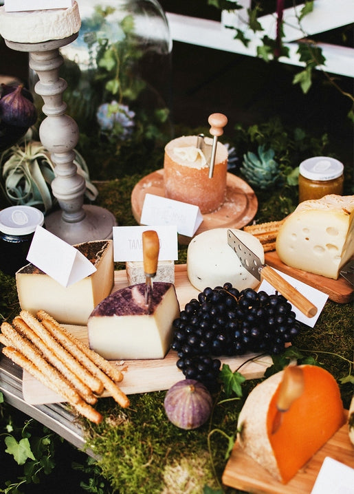 Rustic cheese board with wedges of cheese, grapes, figs and breadsticks set outdoors on moss