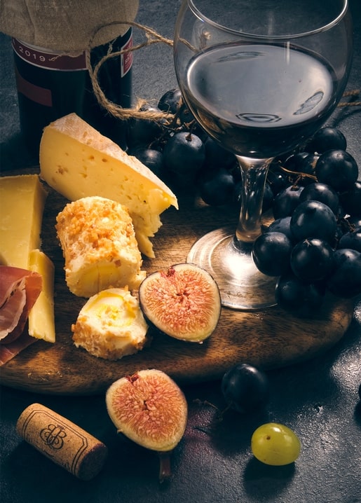 Käse, Prosciutto, Feigen und Trauben auf einem Holzbrett neben einem Glas Rotwein