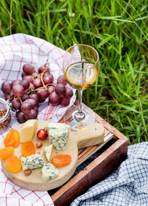 Cheese board with dried apricots, grapes and white wine on a picnic blanket