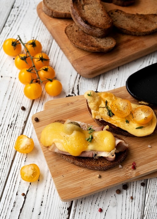 Melted cheese toast with ham and cherry tomatoes on a wooden board