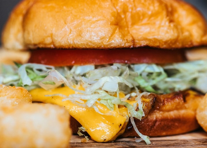 Close-up of a cheeseburger with melted cheese, lettuce, and tomato beside tater tots