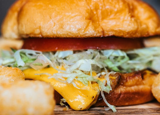Cheeseburger in Nahaufnahme mit geschmolzenem Käse, Salat und Tomate neben Kartoffelecken
