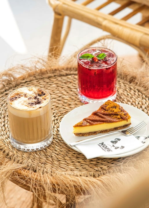 Cheesecake, Latte und Beerengetränk auf einem Rattan-Café-Tisch