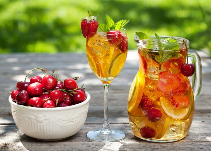 Schale mit Kirschen neben einem Krug eisgekühlter Fruchtlimonade