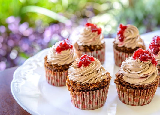 Schokoladen-Cupcakes mit Sahnehaube und glänzender Kirschkonfitüre auf weißem Teller
