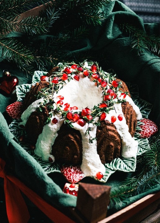 Bundt cake with white icing and a pomegranate-seed wreath among pine branches