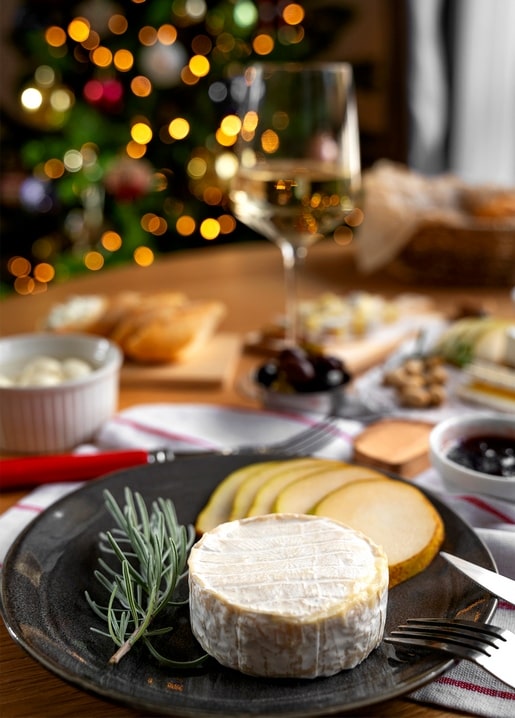 Soft cheese, pear slices and a glass of white wine on a table with a blurred Christmas tree