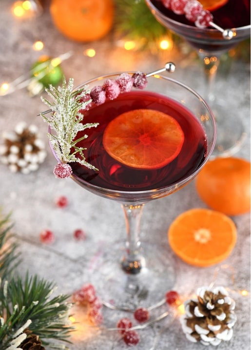 Ruby-red Christmas cocktail garnished with orange slice and sugared cranberries