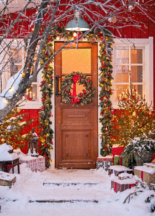 Snowy front door decorated with a wreath, fir garland, and warm string lights