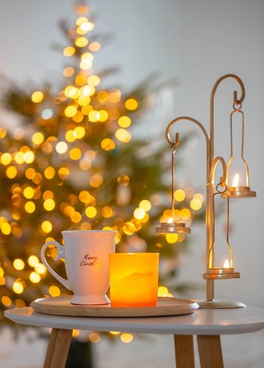 Mug, candle and hanging tealight lanterns in front of a blurred Christmas tree