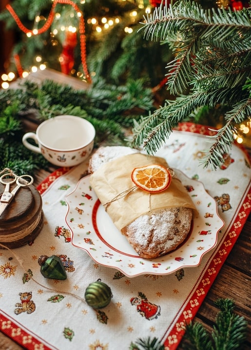 Powdered stollen with dried orange slice on a plate beside a teacup under a Christmas tree