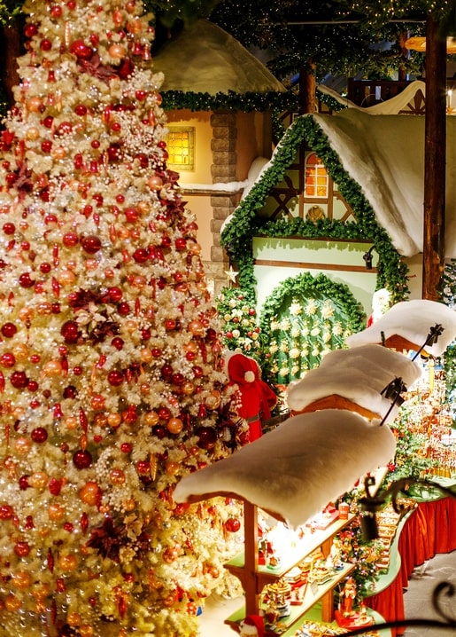 Gold and red Christmas tree beside a snow-capped wooden market stall at dusk